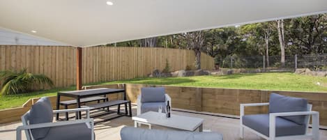 An outdoor patio area with a wooden deck, a table with chairs, and a sofa.