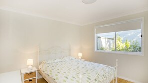 Une chambre avec un lit simple, deux tables de chevet avec des lampes, une fenêtre donnant sur un paysage verdoyant et un plafond blanc.