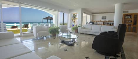 A spacious living area with a large glass window overlooking the ocean, white furniture, and a modern design.