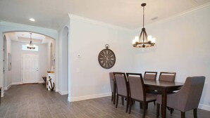 A dining area with a wooden table and chairs, a wall clock, and a chandelier. - 3BR villa in gated community w/tons of amenities! Villa Eleadora - SWFL Rentals (Cape Coral)