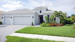 A modern two-story house with a garage, a well-maintained lawn, and a small garden with tropical plants. - 3BR villa in gated community w/tons of amenities! Villa Eleadora - SWFL Rentals (Cape Coral)