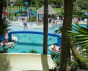 Un área de piscina con tobogán, sillas de descanso y un parque infantil.