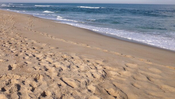 A beach with footprints leading to the water, a clear sky, and waves approaching the shore. - 2nd floor of duplex. Bay view, sunsets, beach, activities. Great family getaway! (Ship Bottom)