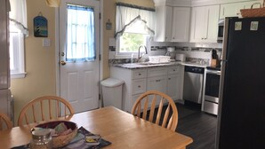 A compact kitchen with white cabinets, a black refrigerator, and a dining table with chairs. - 2nd floor of duplex. Bay view, sunsets, beach, activities. Great family getaway! (Ship Bottom)