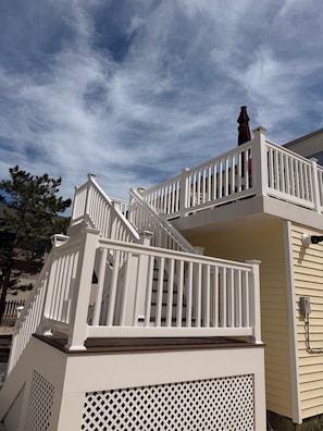 A multi-level white wooden deck with railings, a red umbrella, and a house with beige siding. - 2nd floor of duplex. Bay view, sunsets, beach, activities. Great family getaway! (Ship Bottom)