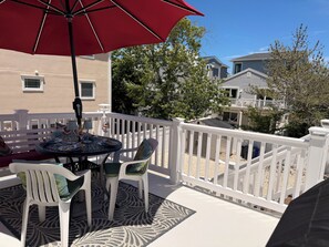 A balcony with a table, chairs, and a red umbrella. - 2nd floor of duplex. Bay view, sunsets, beach, activities. Great family getaway! (Ship Bottom)