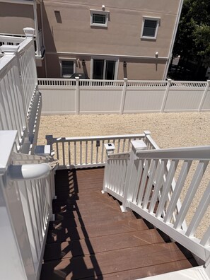 A wooden deck with white railings, a gravel area, and a building with windows and a door. - 2nd floor of duplex. Bay view, sunsets, beach, activities. Great family getaway! (Ship Bottom)