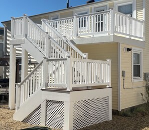 A two-story building with a white exterior, a balcony on the upper floor, and a staircase leading to the second floor. - 2nd floor of duplex. Bay view, sunsets, beach, activities. Great family getaway! (Ship Bottom)