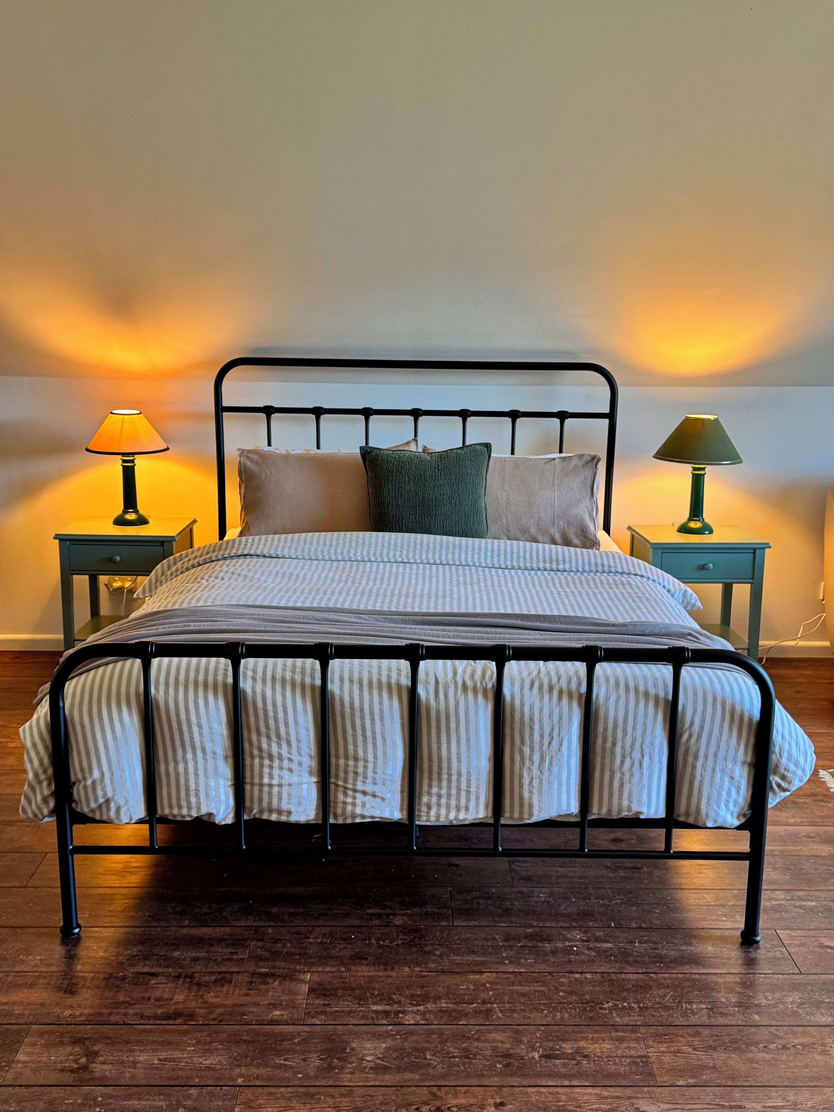 A bed with a metal frame, two bedside tables with lamps, and a wooden floor.