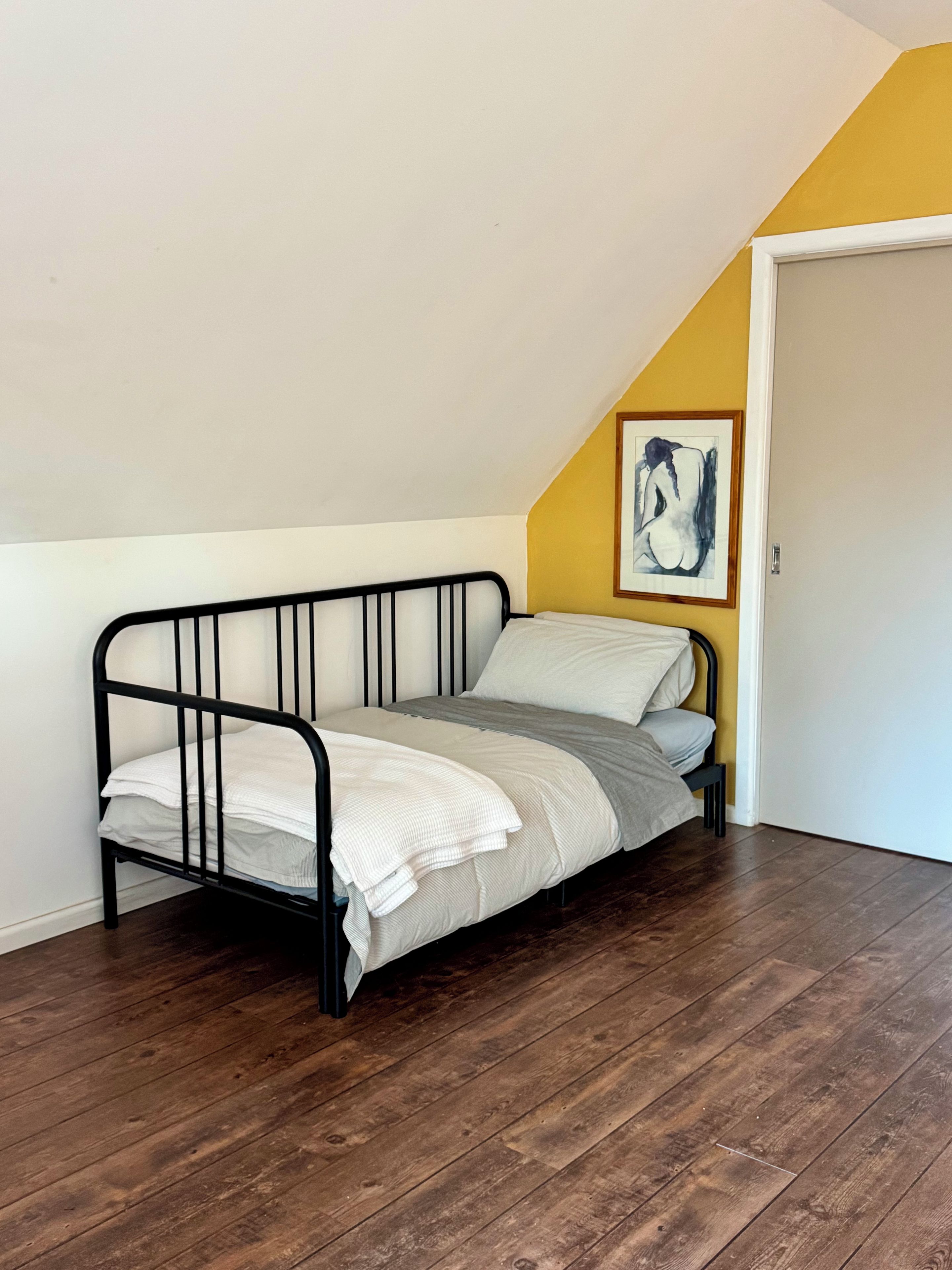 Une petite chambre avec un lit simple, un plafond en pente et un plancher en bois.