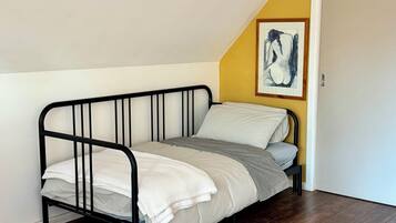Une petite chambre avec un lit simple, un plafond en pente et un plancher en bois.