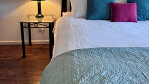 Een netjes opgemaakt bed met een gewatteerde spreidekbed, een bedlampje en een nachtkastje met een lamp.
