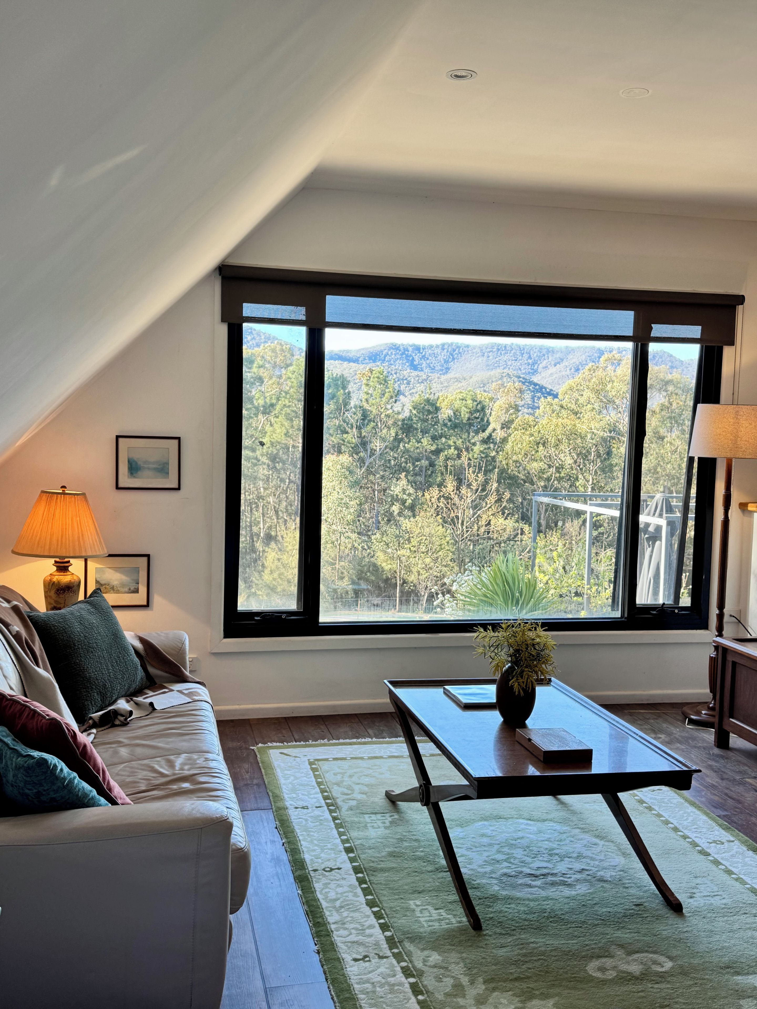 Une pièce avec une grande fenêtre, un canapé, une table et une lampe.