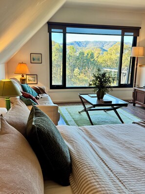 A bedroom with a large window, a bed, a sofa, a table, and a lamp.
