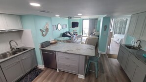 Una cucina compatta con isola centrale, un'area pranzo con divano e vista su una camera da letto.