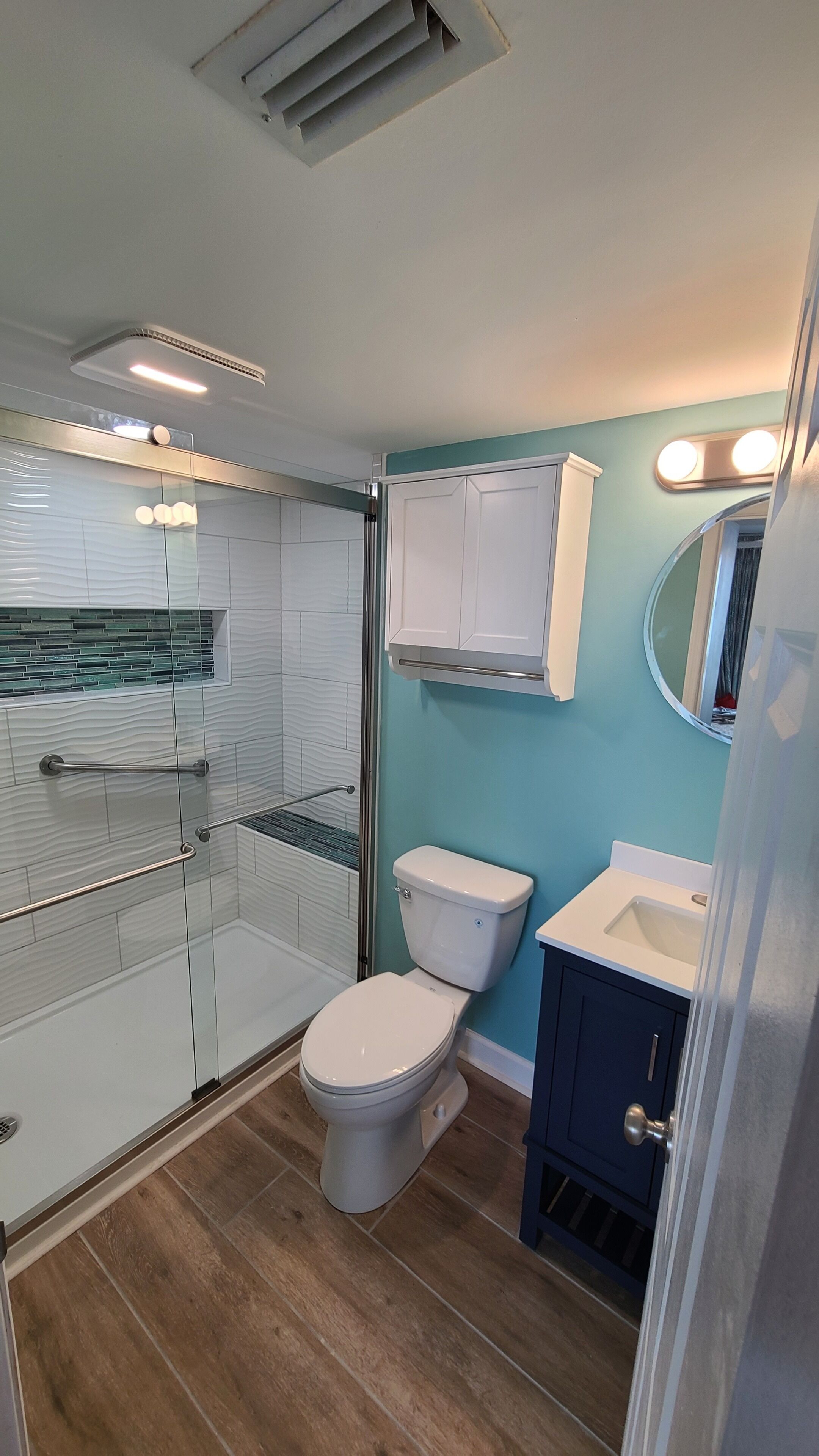 A bathroom with a glass shower enclosure, a white toilet, a sink with a mirror, and a cabinet.