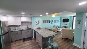 Una cucina moderna con mobili grigi, un'isola in marmo e un'area pranzo con tavolo in vetro e sedie in vimini.