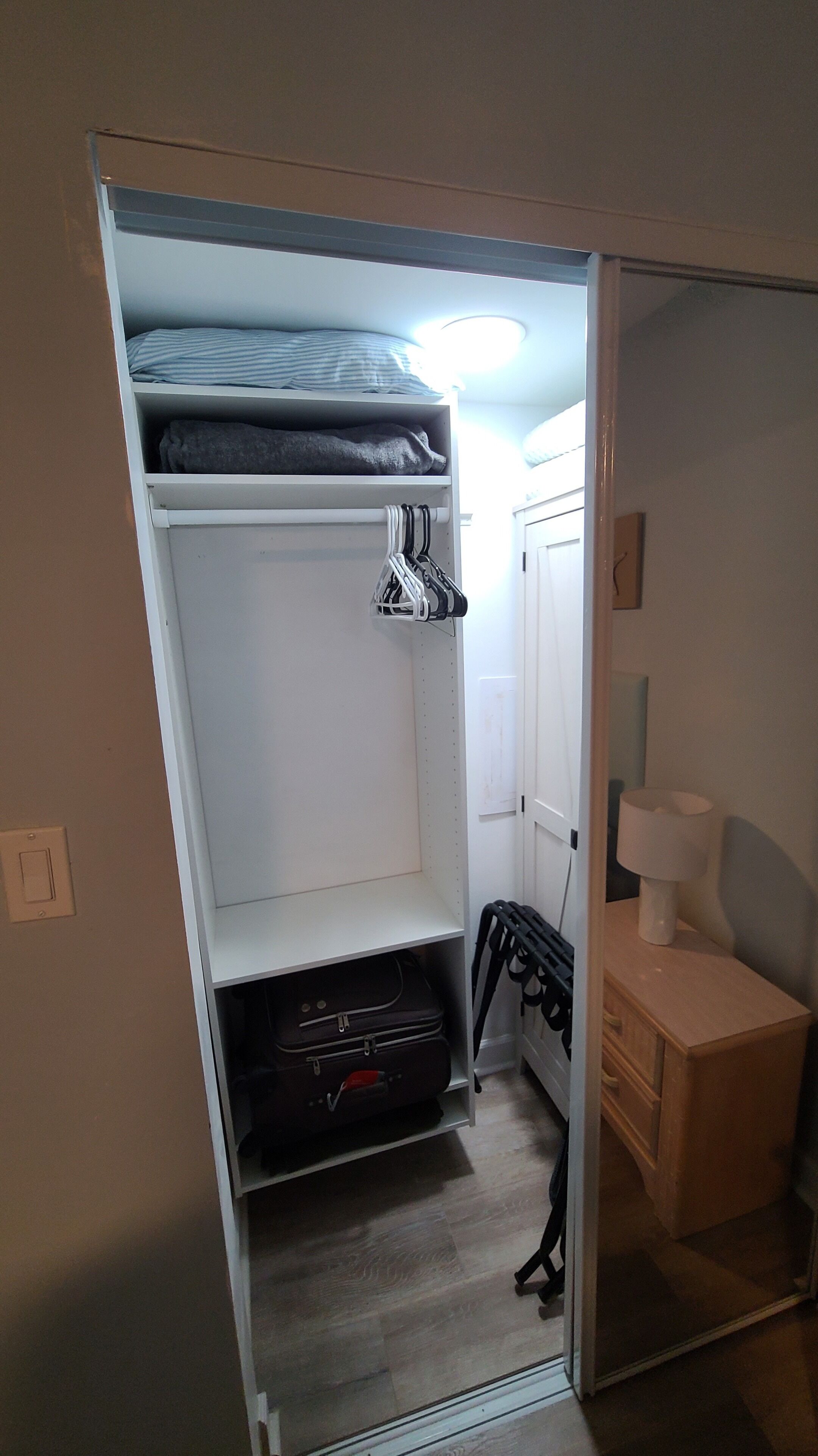 A compact room with a bunk bed, a small kitchenette, and a bedside table with a lamp.