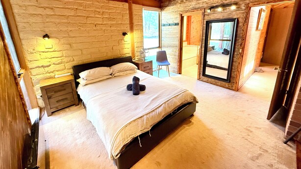 A bedroom with a large bed, a wooden ceiling, and a stone wall. - Grampians Private Bushland Retreat (Halls Gap)
