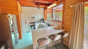 A compact kitchen with a central island, bar stools, and a window overlooking greenery. - Grampians Private Bushland Retreat (Halls Gap)