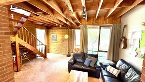 A spacious living area with a wooden staircase, a leather sofa, and a dining table. - Grampians Private Bushland Retreat (Halls Gap)