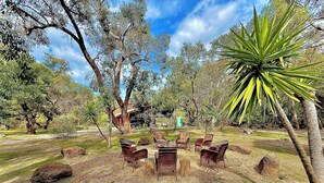 An outdoor seating area with wicker chairs and a central table, surrounded by trees and rocks. - Grampians Private Bushland Retreat (Halls Gap)
