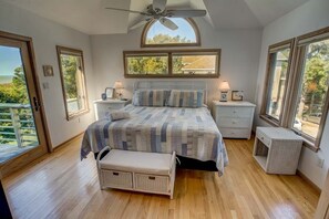Une chambre à coucher avec un lit, des tables de chevet, un banc et de grandes fenêtres.
