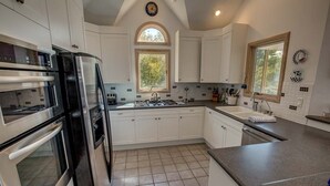 A modern kitchen with white cabinets, stainless steel appliances, and a large window. - Sound's Great! | Sound Front | Private Pool | Corolla (Corolla)