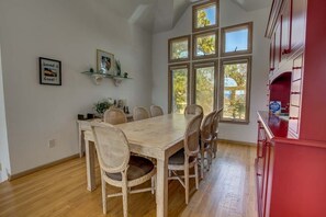 Un coin repas avec une table en bois et des chaises en osier, de grandes fenêtres et un buffet rouge.
