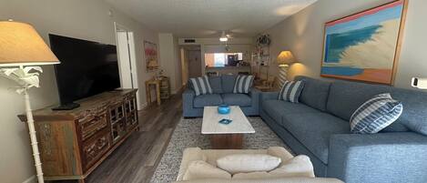 A living room with a sectional sofa, a TV, a coffee table, and a lamp.