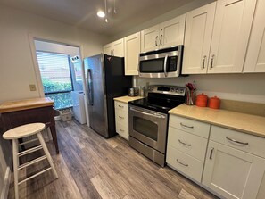 A modern kitchen with stainless steel appliances, white cabinets, and a wooden floor. - Beach Inspired, Eclectic Garden View (Siesta Key)