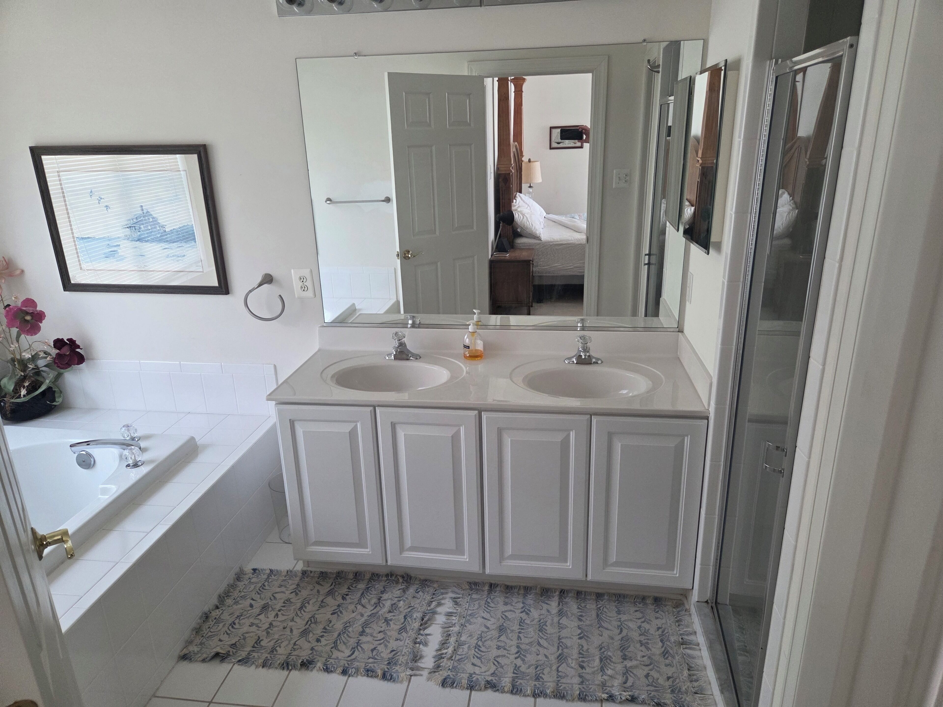Un bagno con doppio lavabo, una vasca da bagno, uno specchio grande e un quadro appeso al muro.