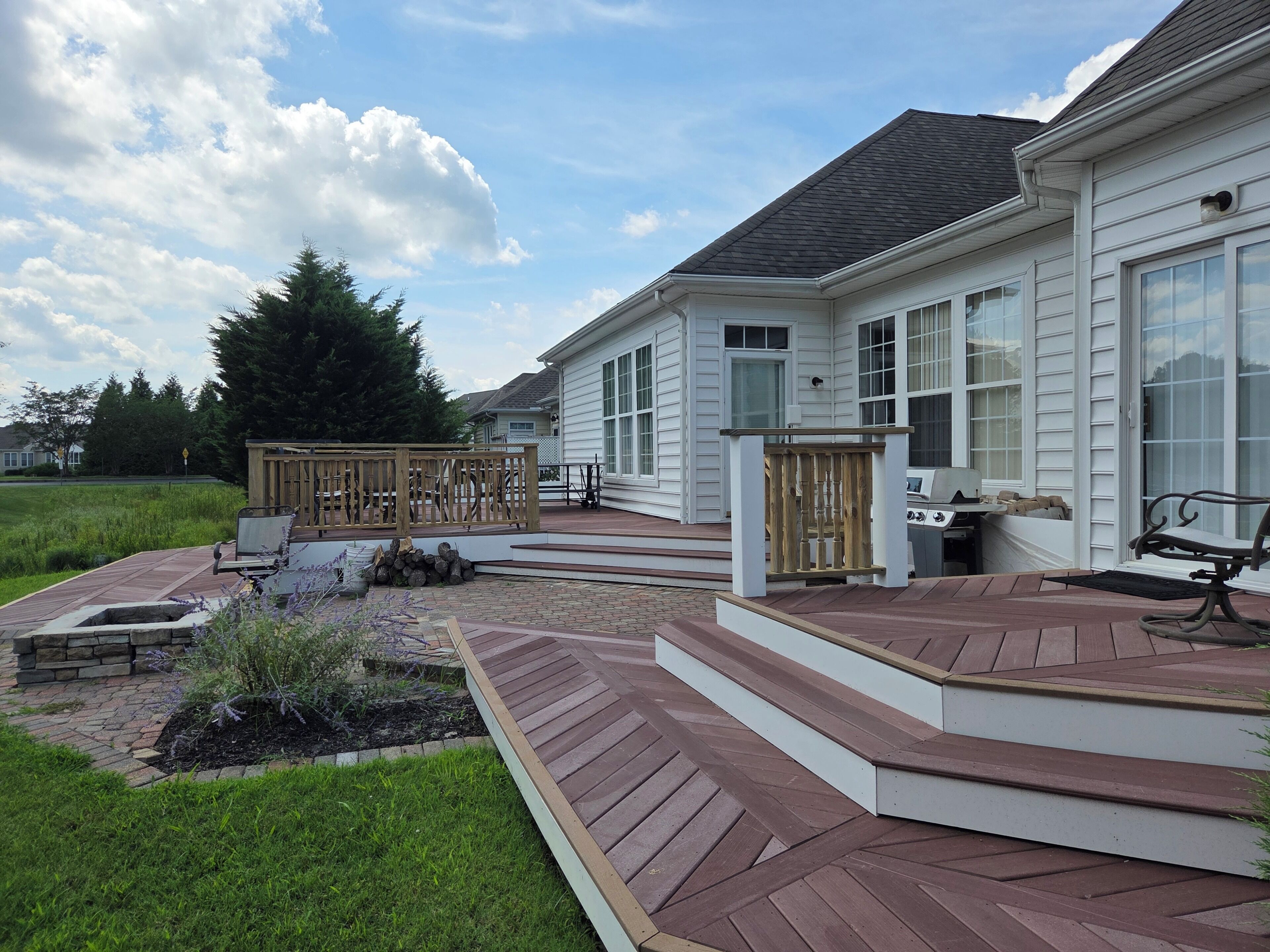 Une terrasse résidentielle dotée d’un foyer extérieur, de sièges et offrant une vue sur une maison aux grandes fenêtres.