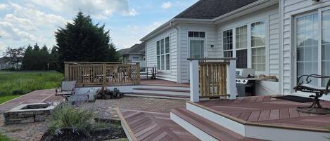 A residential deck with a fire pit, outdoor seating, and a view of a house with large windows.