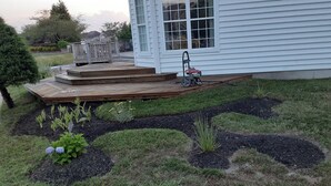 Een huis met een houten terras, een gazon en een tuin met diverse planten.