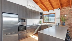 A modern kitchen with stainless steel appliances, a wooden ceiling, and a brick wall. - Beachcombers on Collingwood Beach (Vincentia)
