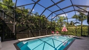 En swimmingpool med et geometrisk glasomslutning, omgivet af palmer og en klar himmel.