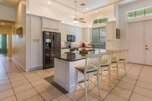 Una cucina moderna con mobili bianchi, un'isola centrale con posti a sedere e una ventola a soffitto.