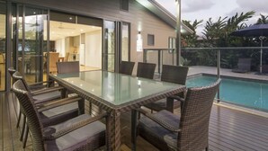Un espace repas extérieur avec une table en verre et des chaises en osier, donnant sur une piscine.