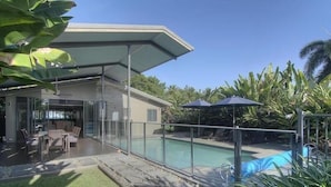 Une maison moderne dotée d’un patio entièrement vitré, d’une piscine et d’une végétation tropicale luxuriante.