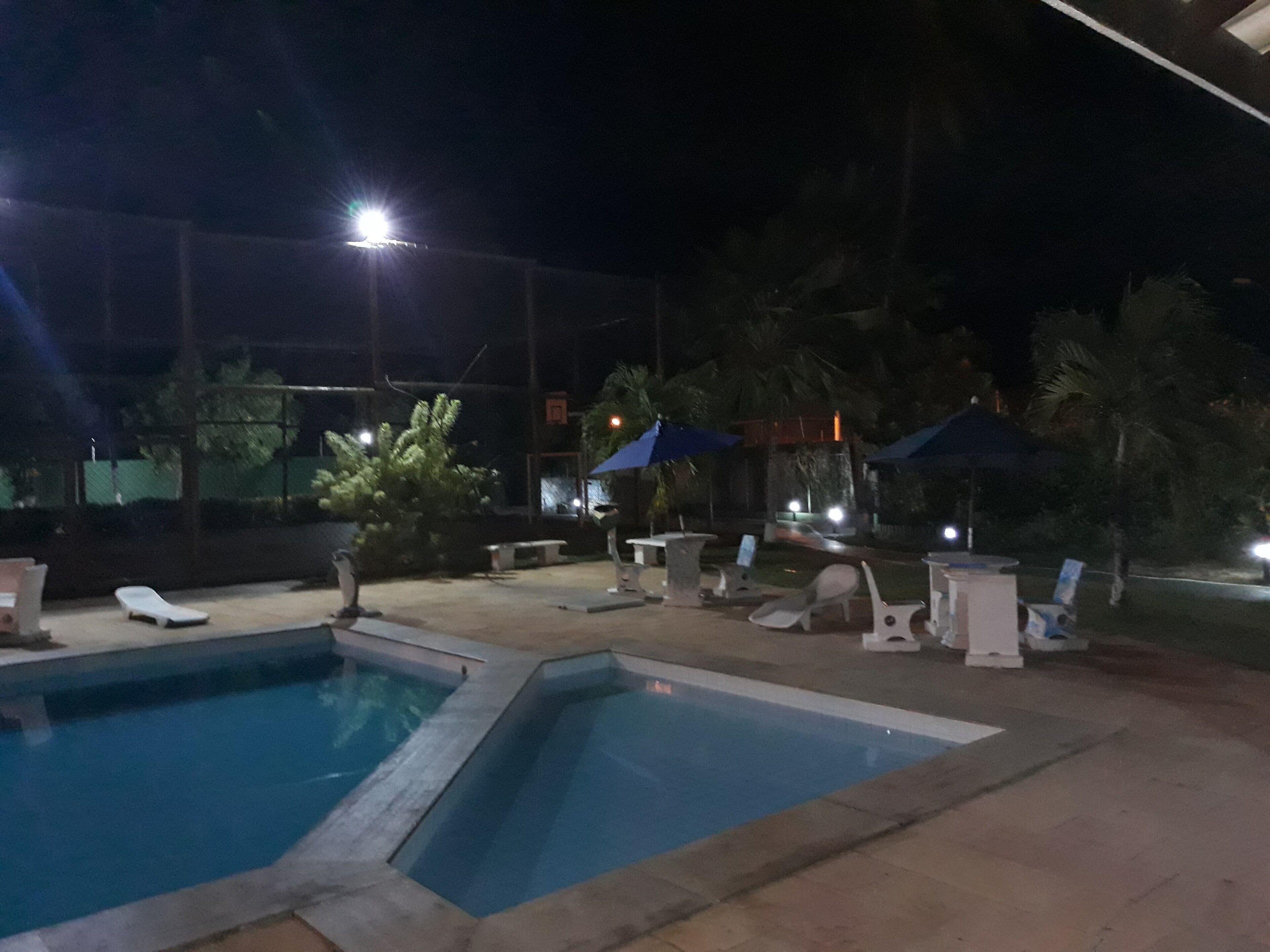 A nighttime pool area with lounge chairs and umbrellas.