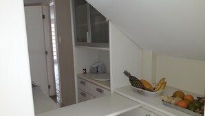 Keittiössä on valkoiset kaapit, työtasolla on hedelmäkulho ja ovi johtaa toiseen huoneeseen.