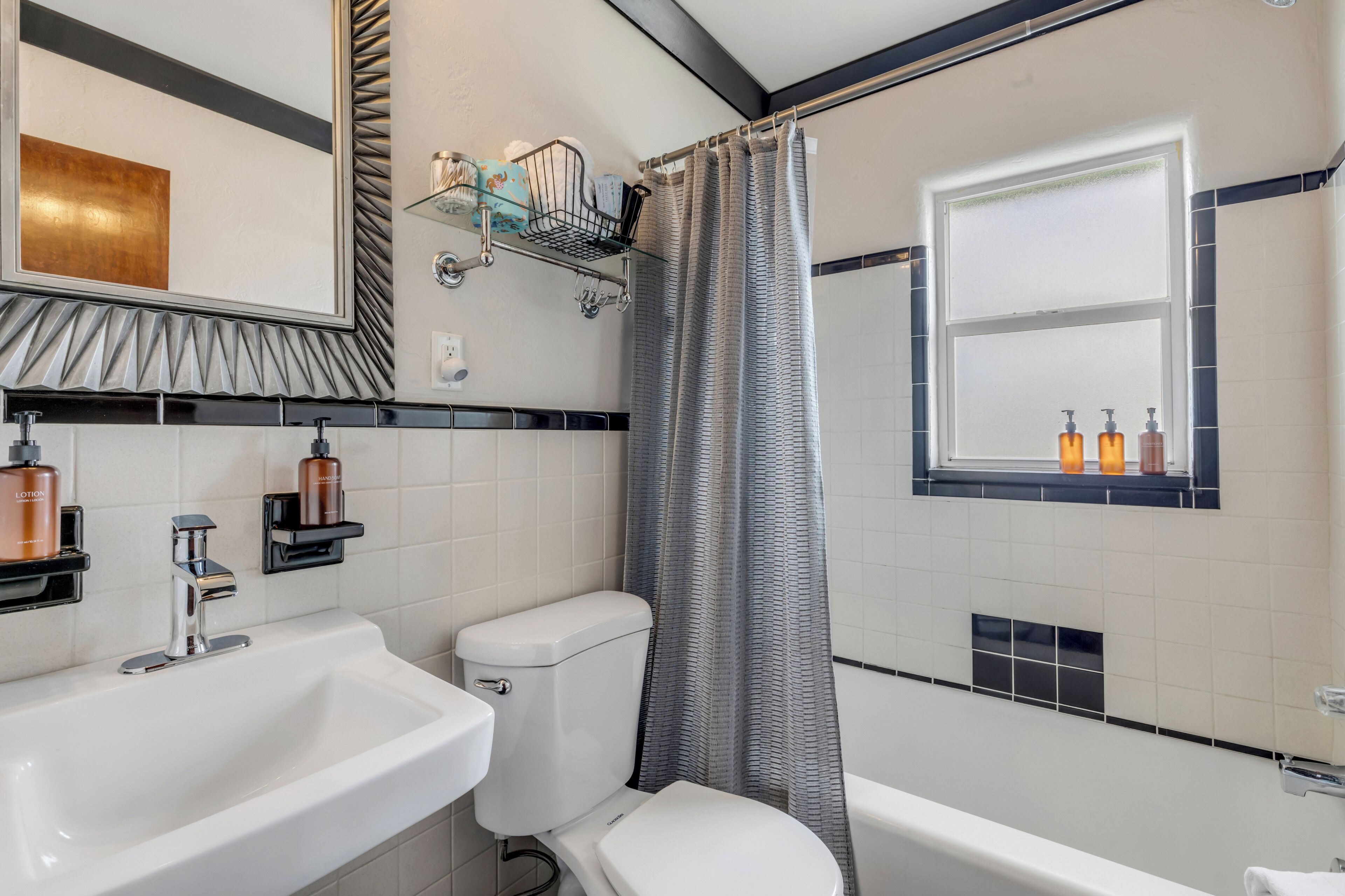 Une salle de bain moderne avec des toilettes, un lavabo et une baignoire. Il y a une fenêtre avec des bouteilles posées sur le rebord.
