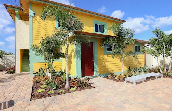 A yellow house with a red door, surrounded by plants and a paved walkway. - Modern Design, Boat Parking, Steps to Intercoastal Access (New Smyrna Beach)