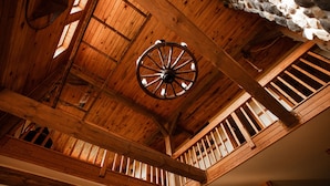 Un intérieur en bois agrémenté d’un grand lustre en forme de roue, de poutres en bois et d’un mur en pierre.