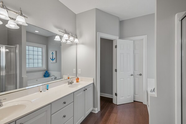 A bathroom with a large mirror, white cabinets, a sink, and a door leading to another room. - A Bushel And A Peck - Pet Friendly, Luxury Channel Home with Fantastic Views and Beautiful Pool Area (NORTH MYRTLE BEACH)