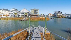 Een pand aan het water met een steiger, een voetgangersbrug en een rij meerhoogbouwwoningen met balkons.