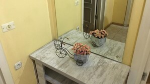 Une salle de bain avec un mur jaune, un miroir, un comptoir en marbre, un pot de fleurs et un récipient en forme de vélo.