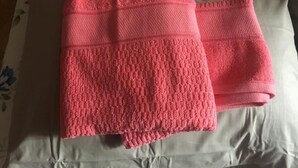 Une couverture rose pliée est posée sur un lit recouvert d’une couvre-lit à motifs floraux.