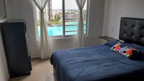 Une chambre à coucher avec un lit, une table de chevet, une fenêtre avec des rideaux et une vue sur une piscine.